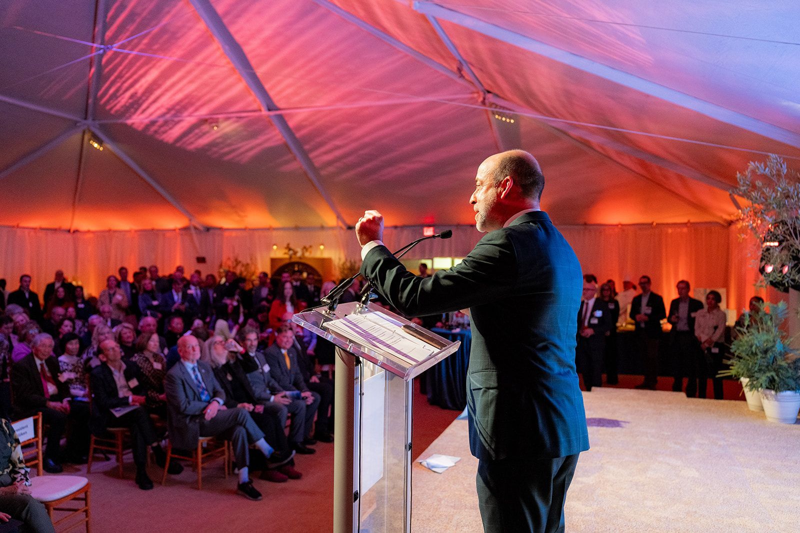 Speaker at podium addressing a seated audience inside a large orange-lit tent. UCI health