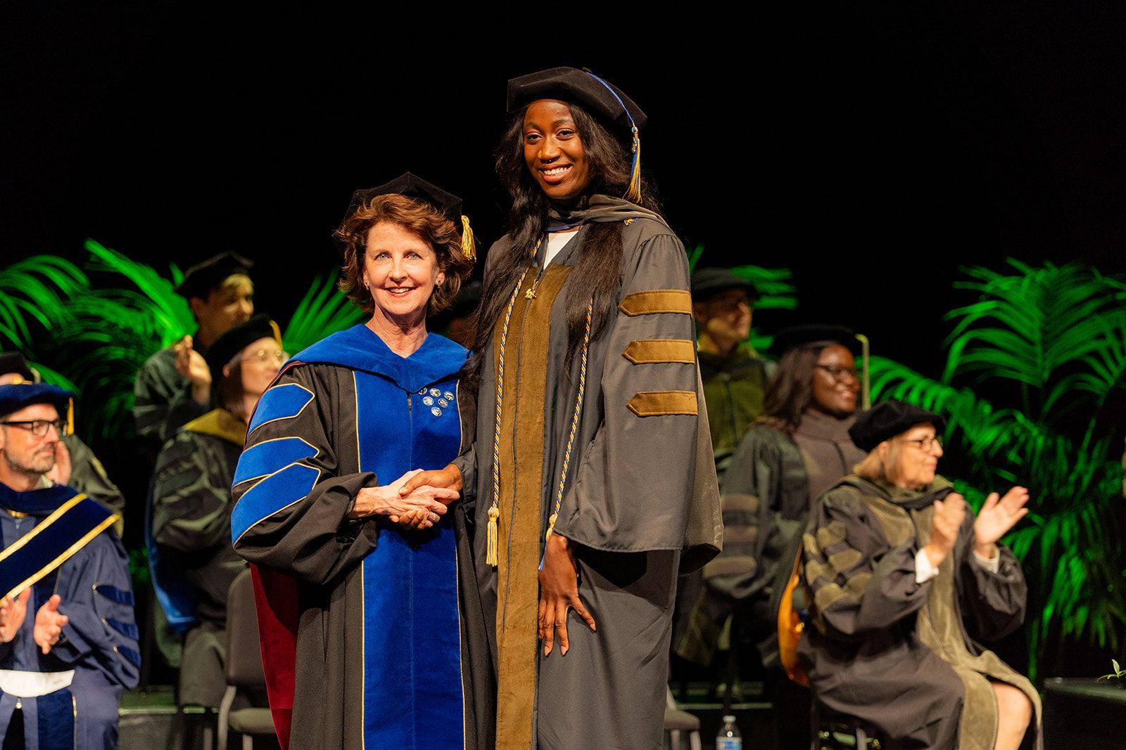 Two people pose onstage in graduation gowns, for UCI Pharmaceutical graduation