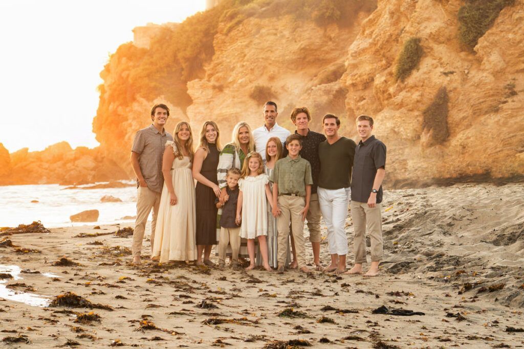 A large family is posing for a picture on the beach.