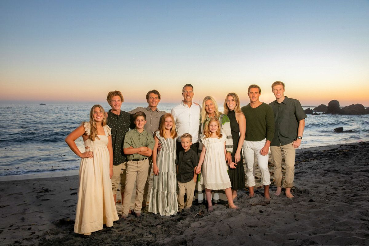 A large family is posing for a picture on the beach at sunset.