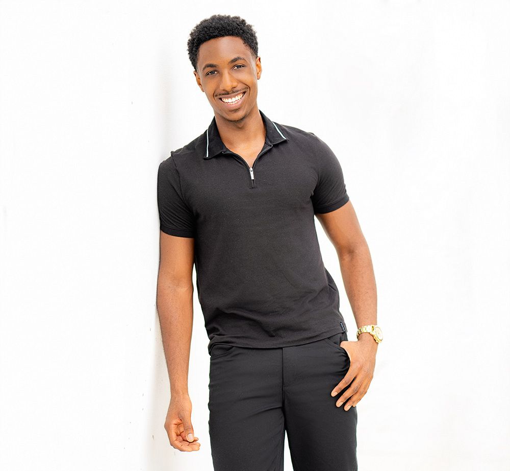 A man smiling for a dating app photo in front of a white wall.