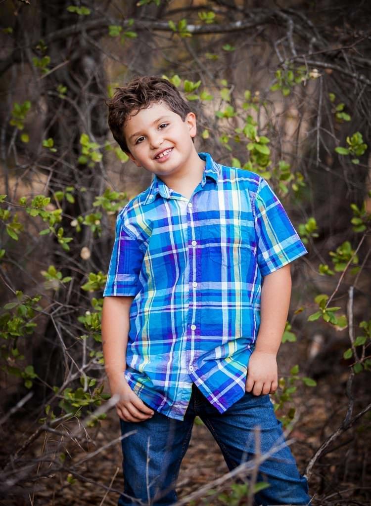 A young boy wearing a blue plaid shirt and jeans is standing in Irvine regional Park. 