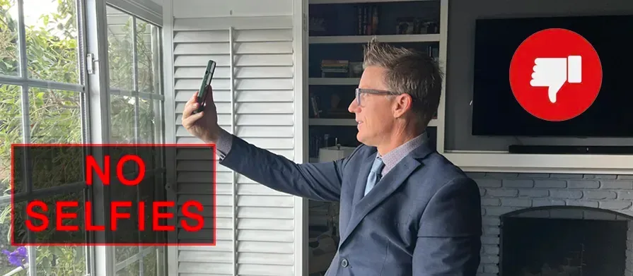 A man in a suit is taking a selfie in front of a window.