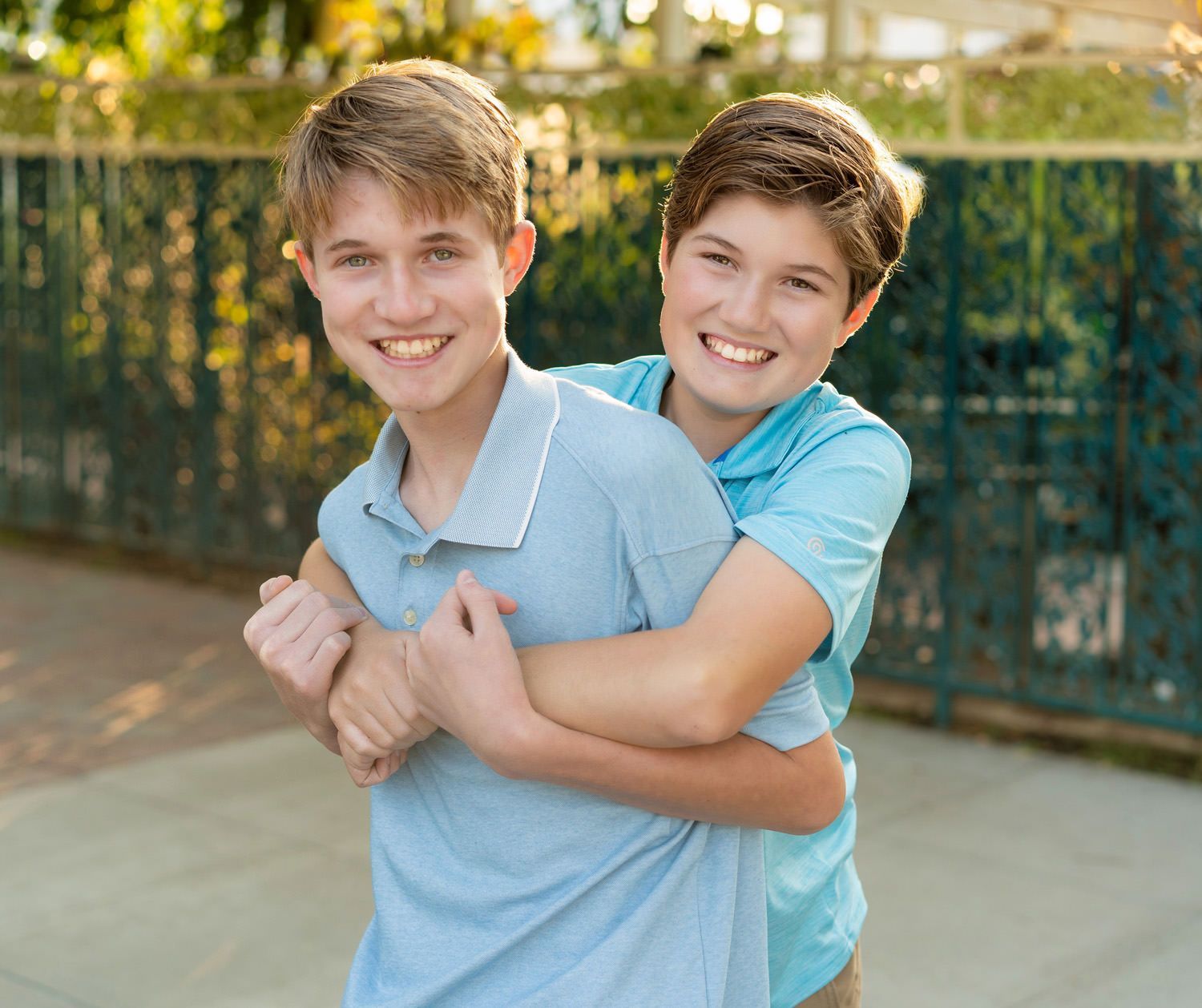Two young brothers hugging each other and smiling for the camera.