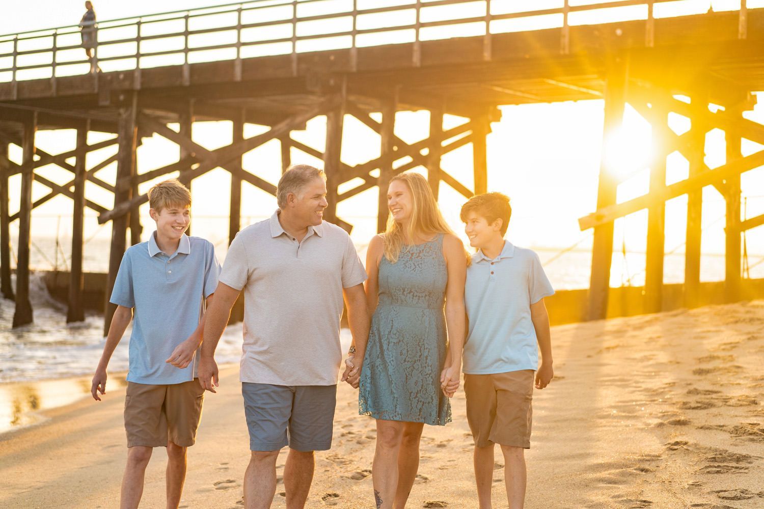 A family is walking on the beach near a pier at sunset in Seal Beach.