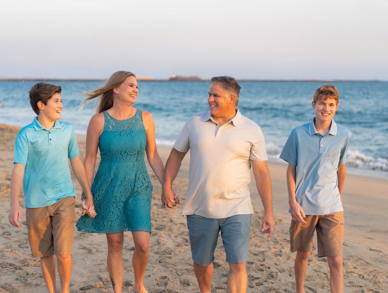 A family is walking on the beach holding hands in Seal Beach. 