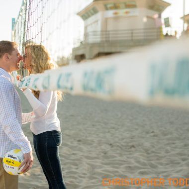 A man and a woman are standing next to a volleyball net on Huntington beach.