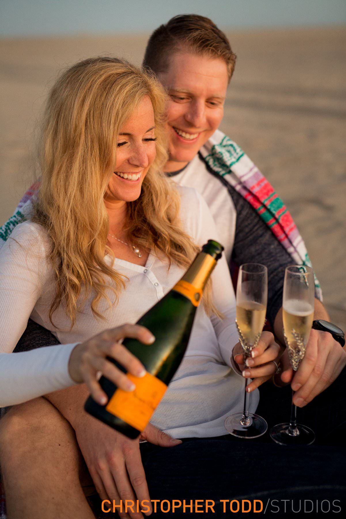 A man is pouring champagne into a glass while a woman holds a bottle of champagne.