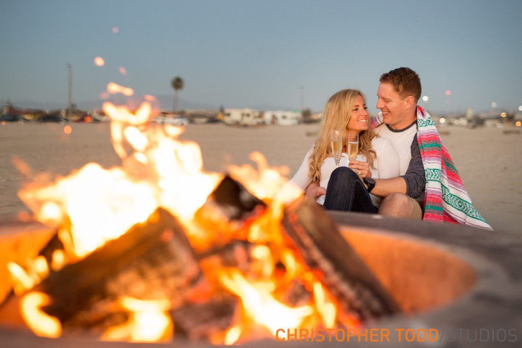 A man and a woman are sitting by a fire on at Huntington Beach