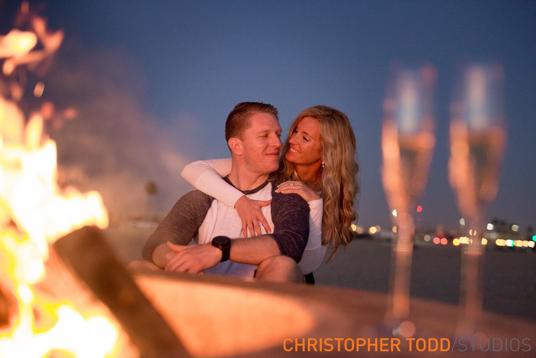 A man and a woman are hugging in front of a fire.