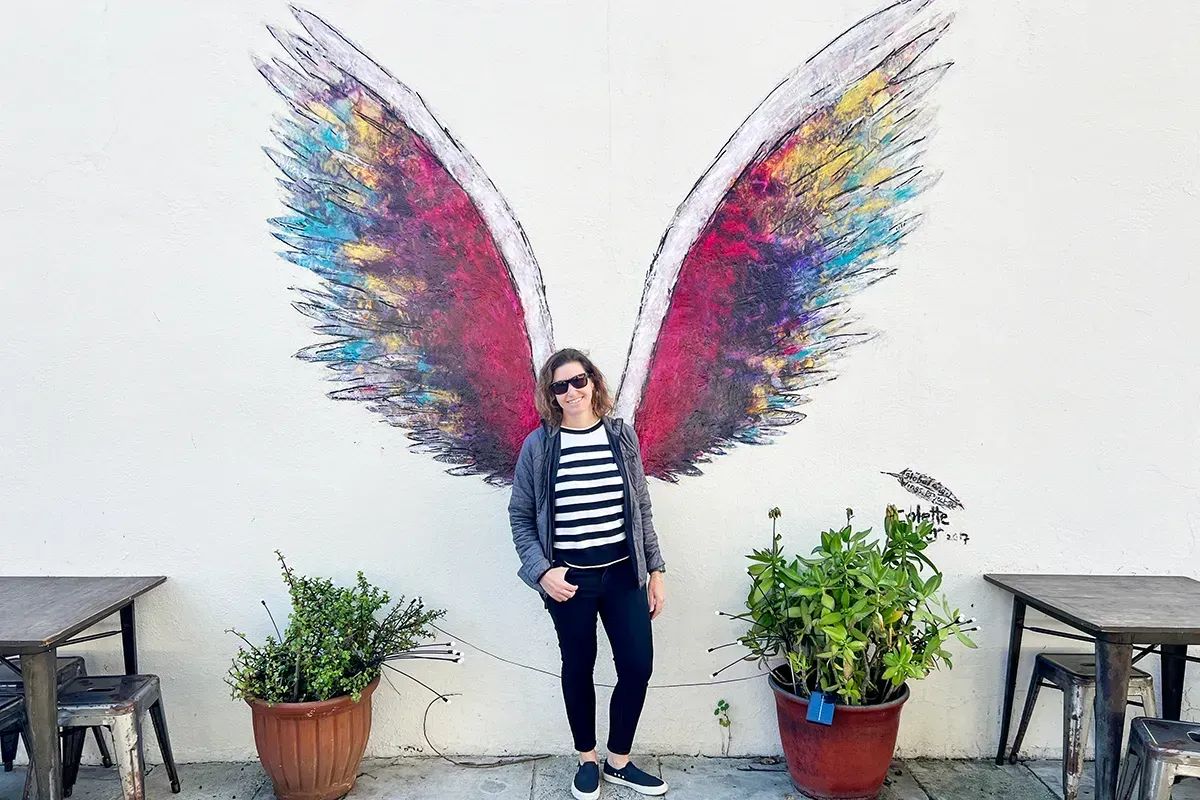 A woman is standing in front of a painting of angel wings at slice pizza in Laguna Beach