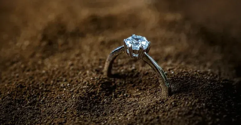 A diamond ring is sitting on top of a pile of sand.