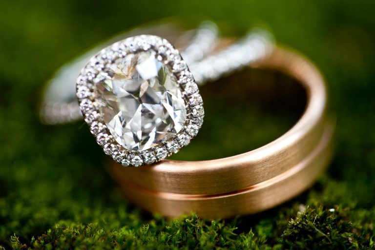 A close up of a wedding ring and engagement ring on a mossy surface.