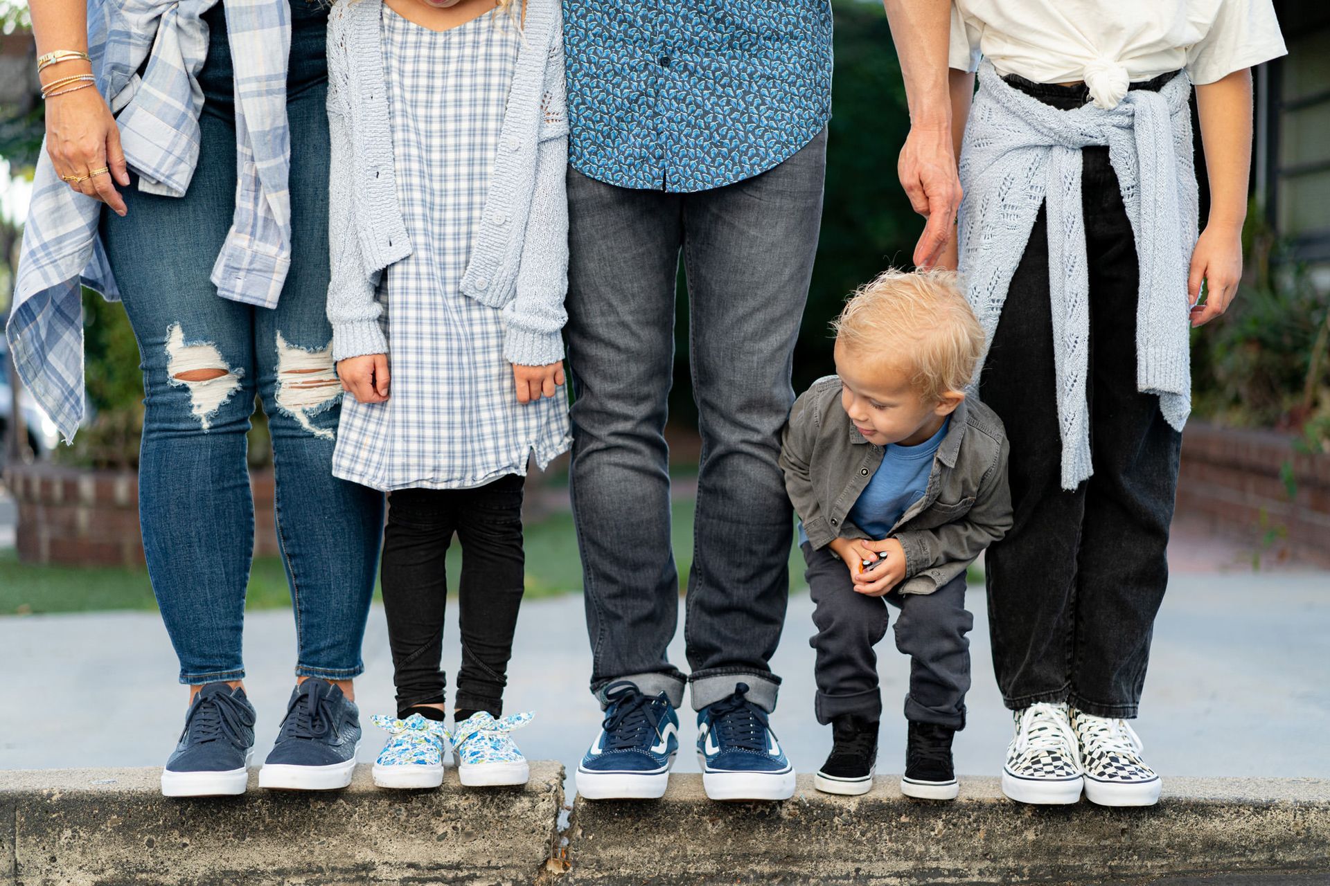 A family is standing beside each other on a sidewalk wearing Vans shoes. 