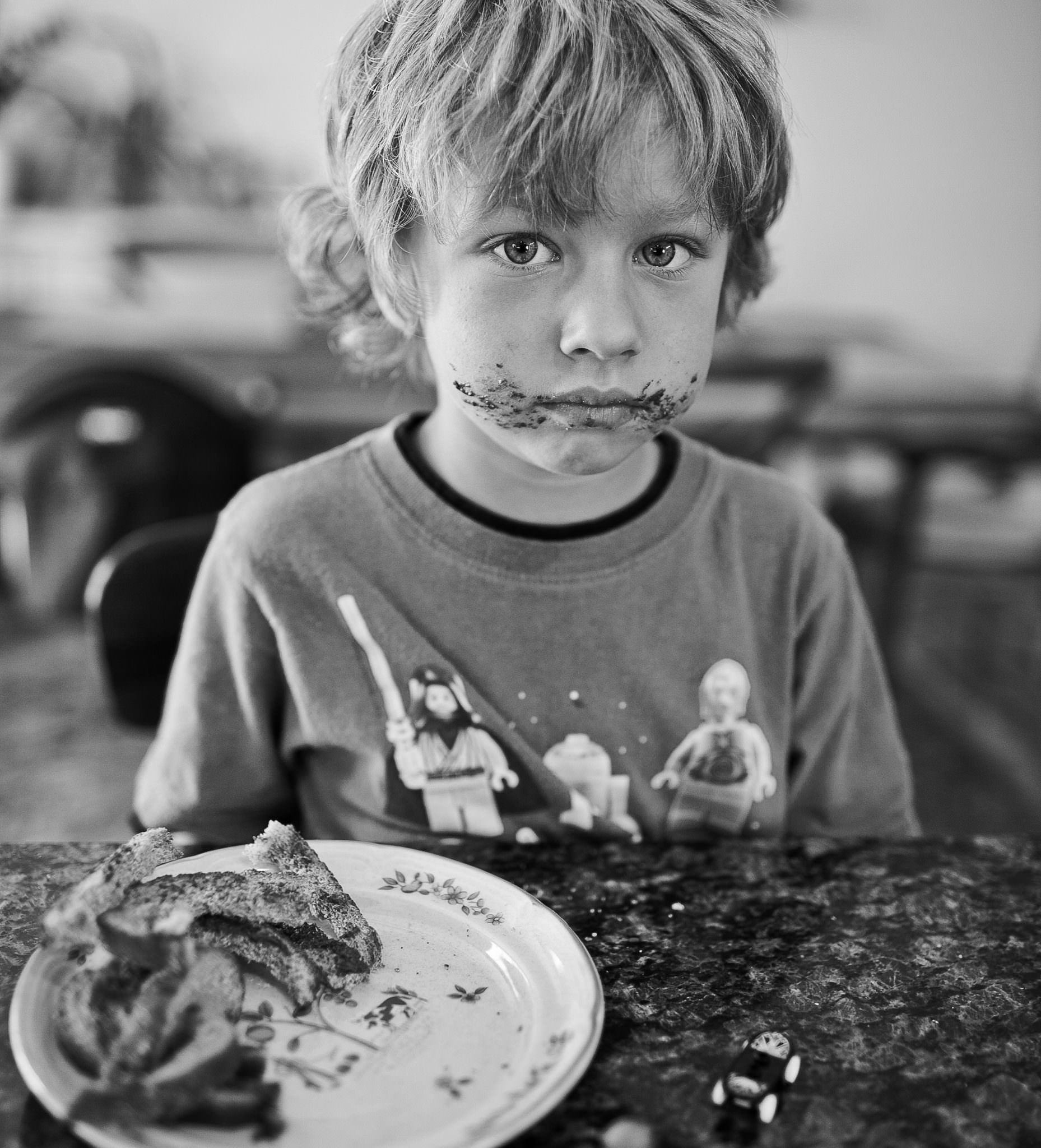 A black and white photo of a young boy sitting at a table with food on his face