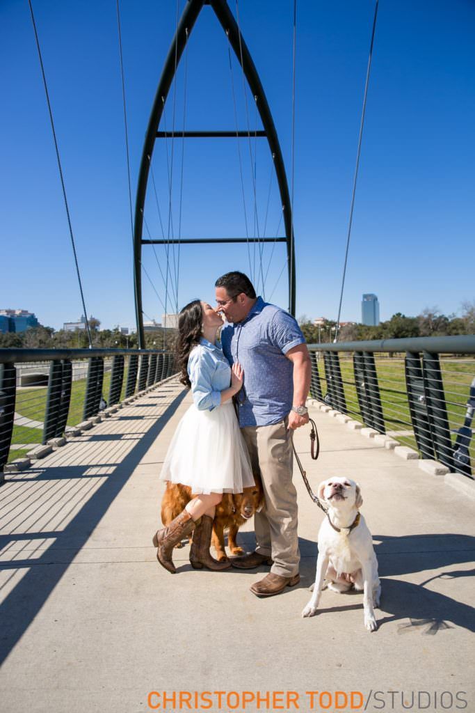 A engaged couple kissing on a bridge with a dog