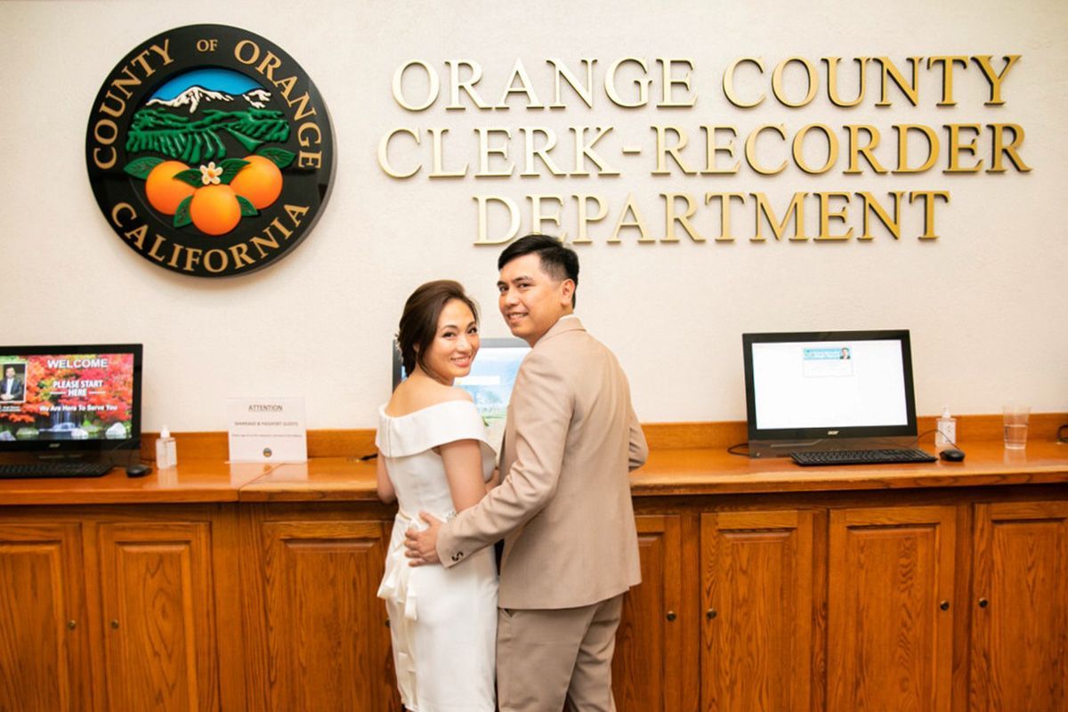 Santa Ana Courthouse Wedding A bride and groom are posing for a picture in front of the orange county clerk recorder department.