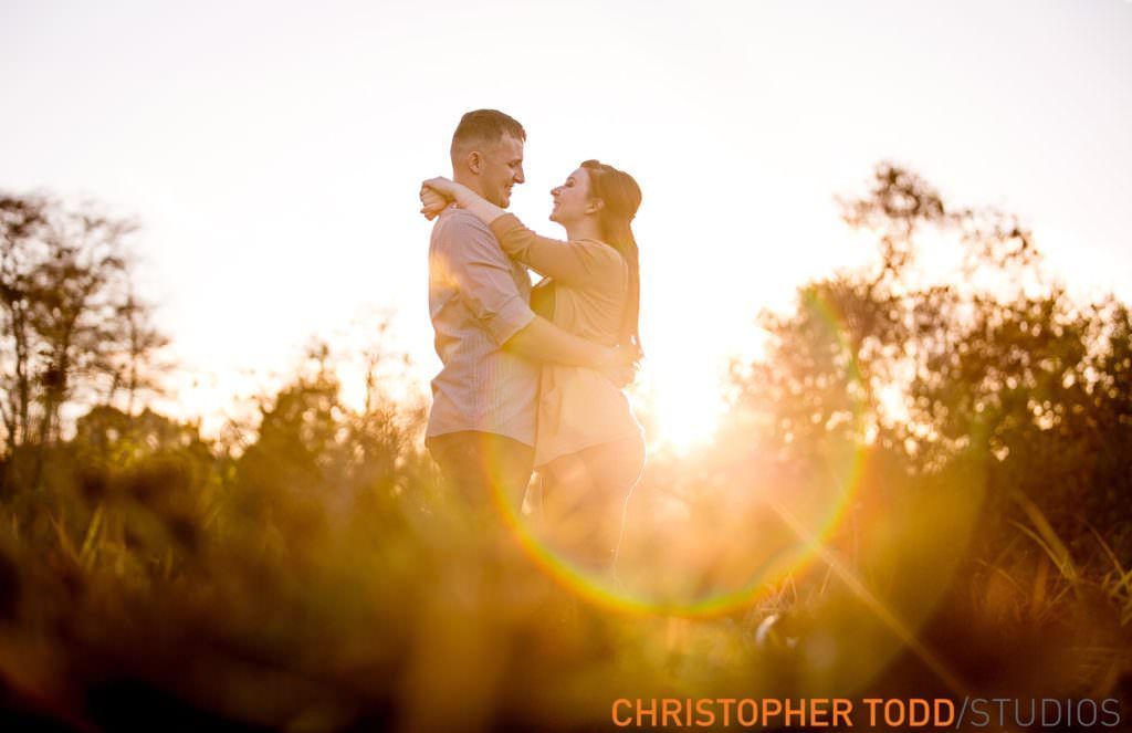 A man and a woman are hugging each other in a field at sunset.