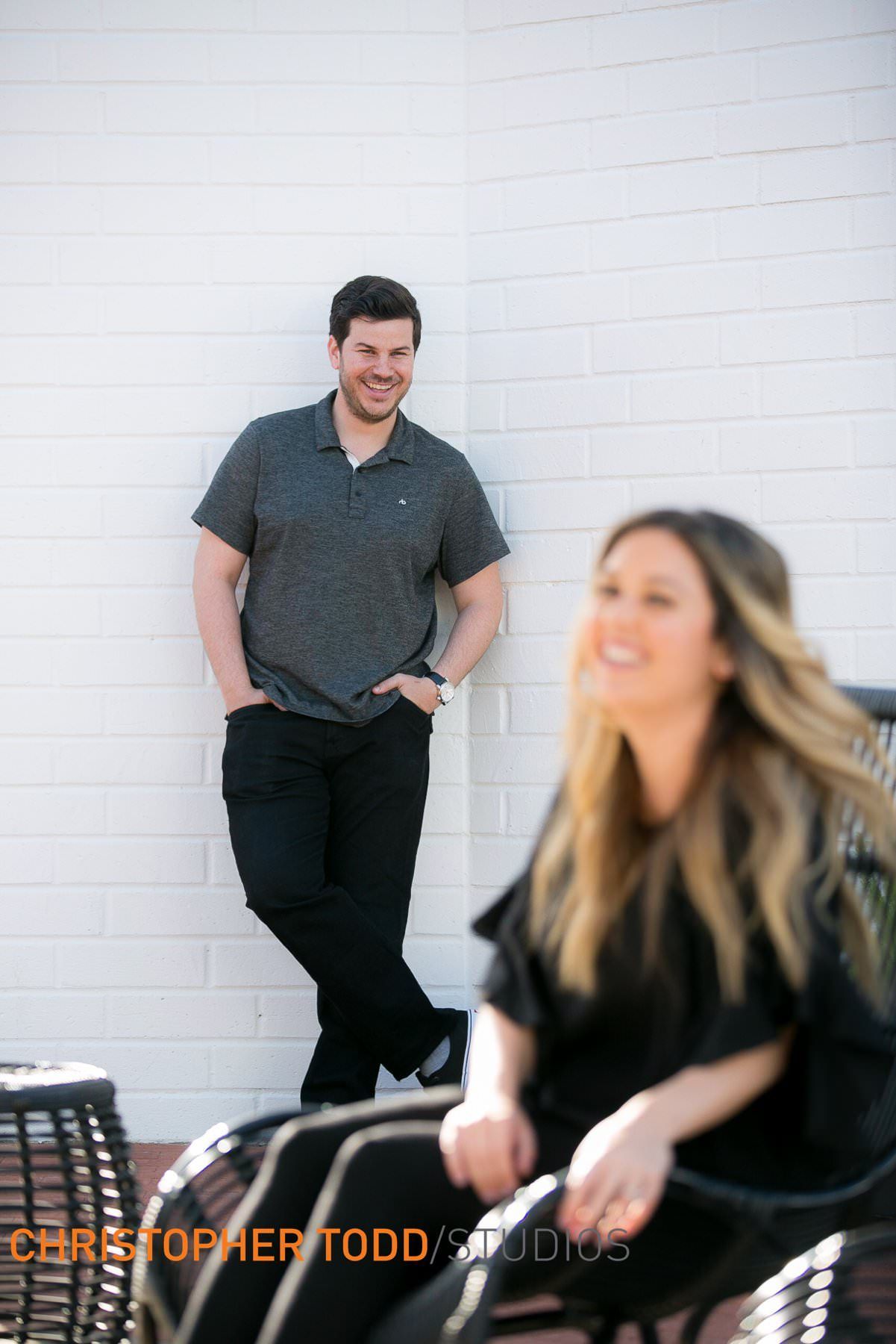 A man and a woman are posing for a picture in front of a white wall.