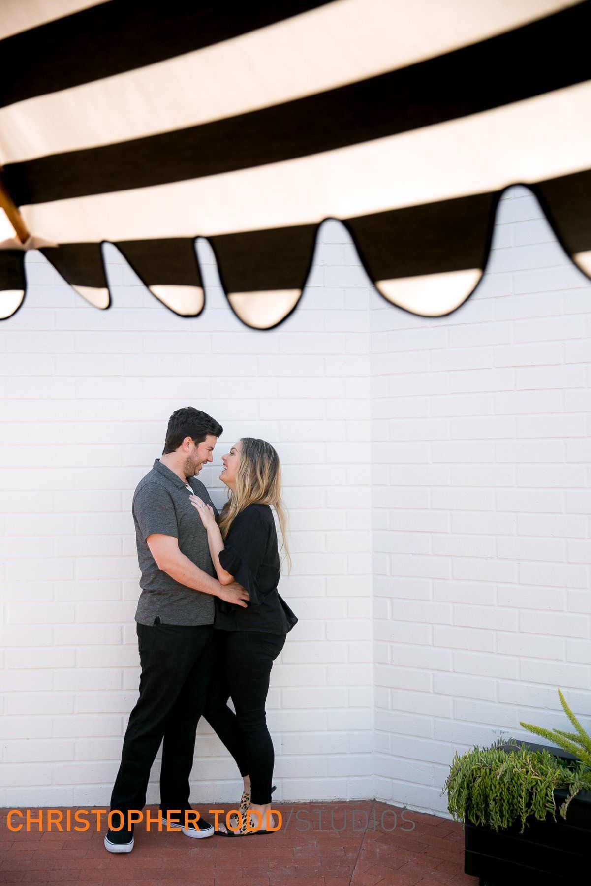 A man and a woman are standing next to each other in front of a white wall.