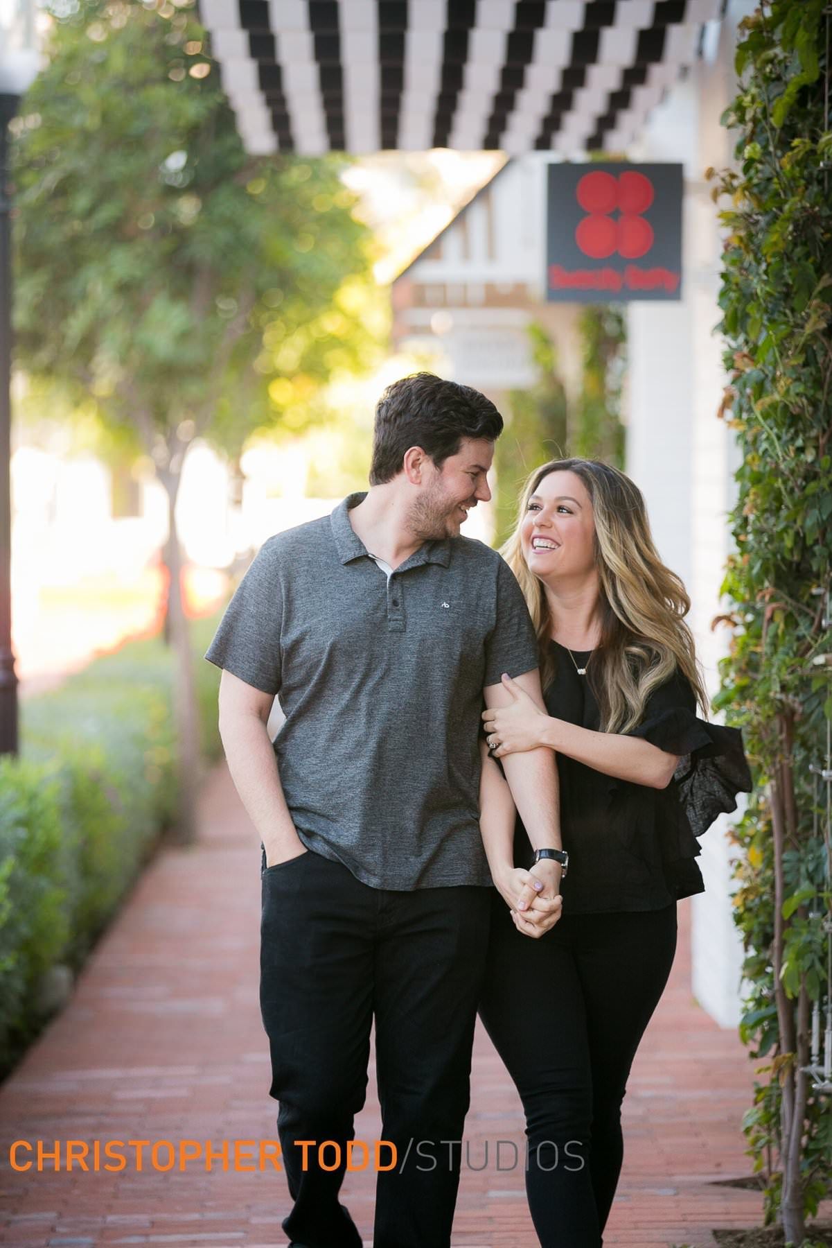 A man and a woman are walking down a sidewalk holding hands.