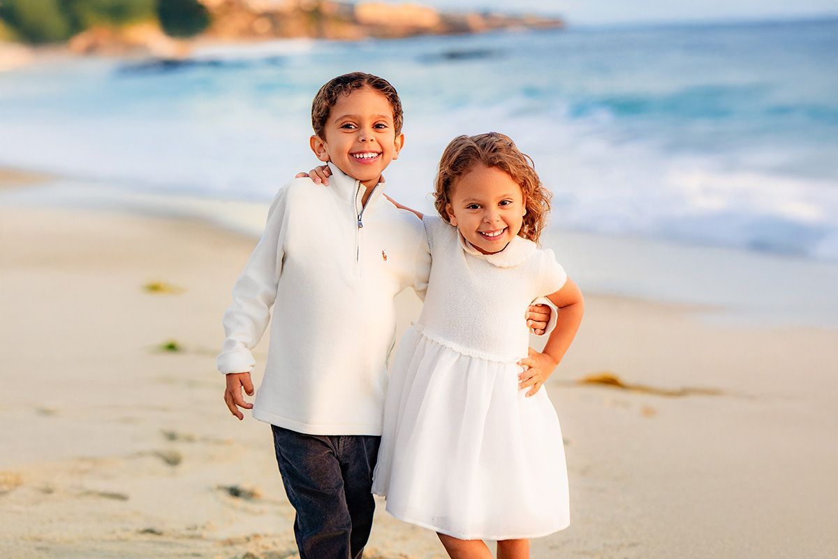 Kids Portraits In Orange County A boy and a girl are standing next to each other on the beach.