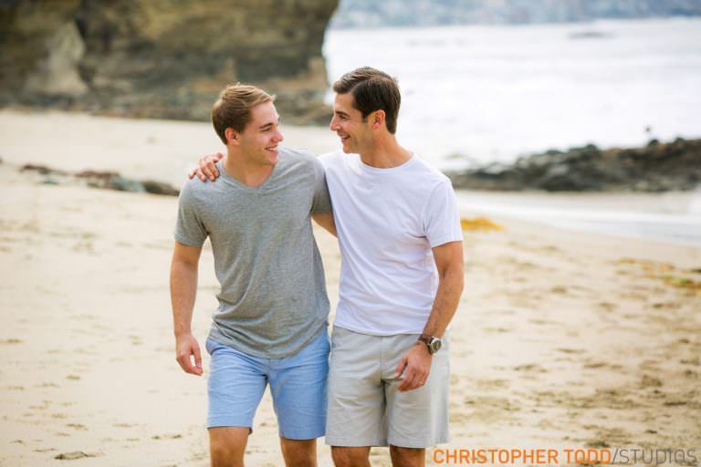 Father and son are walking on the beach with their arms around each other.