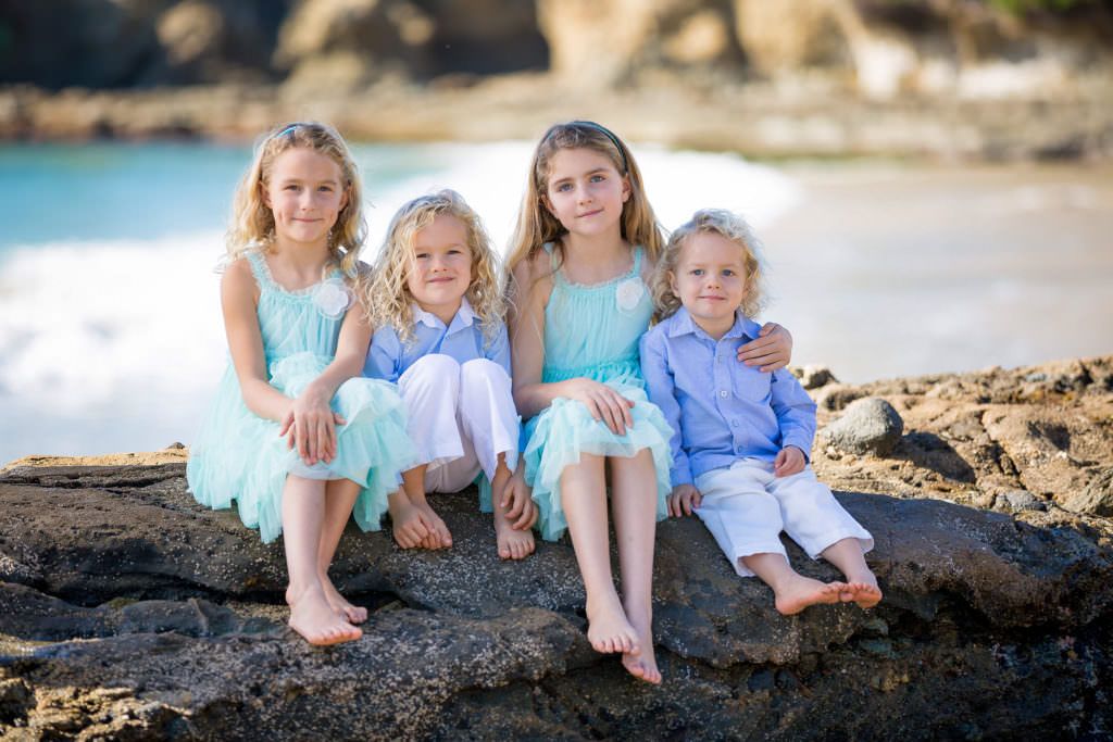 Four young siblings are sitting on a rock on the beach at Laguna Beach.