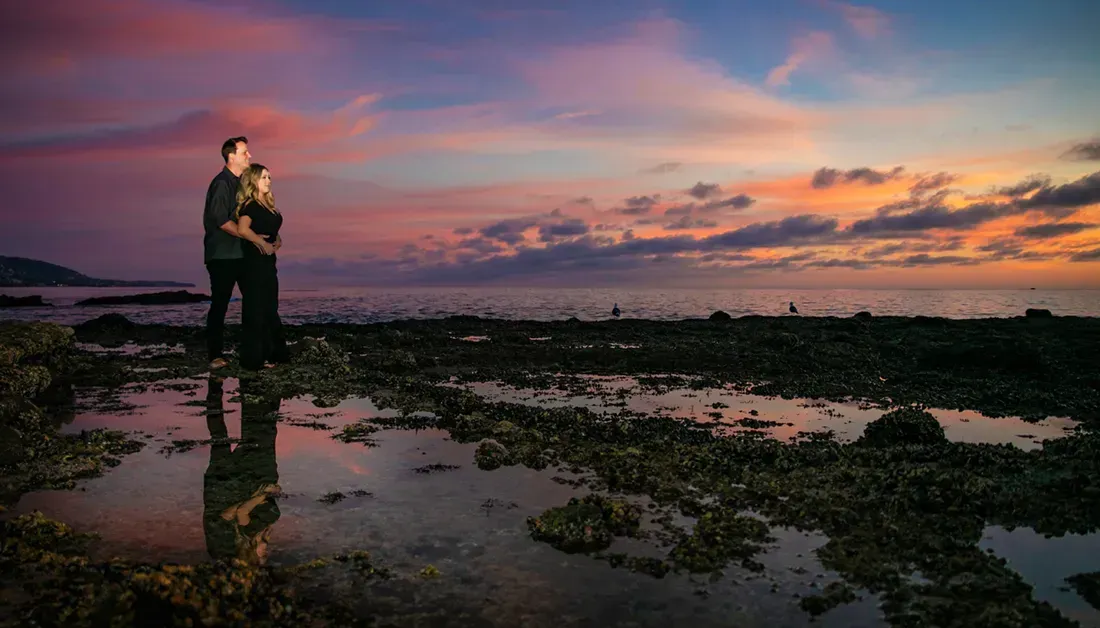 A man and a woman are standing on a beach at sunset.