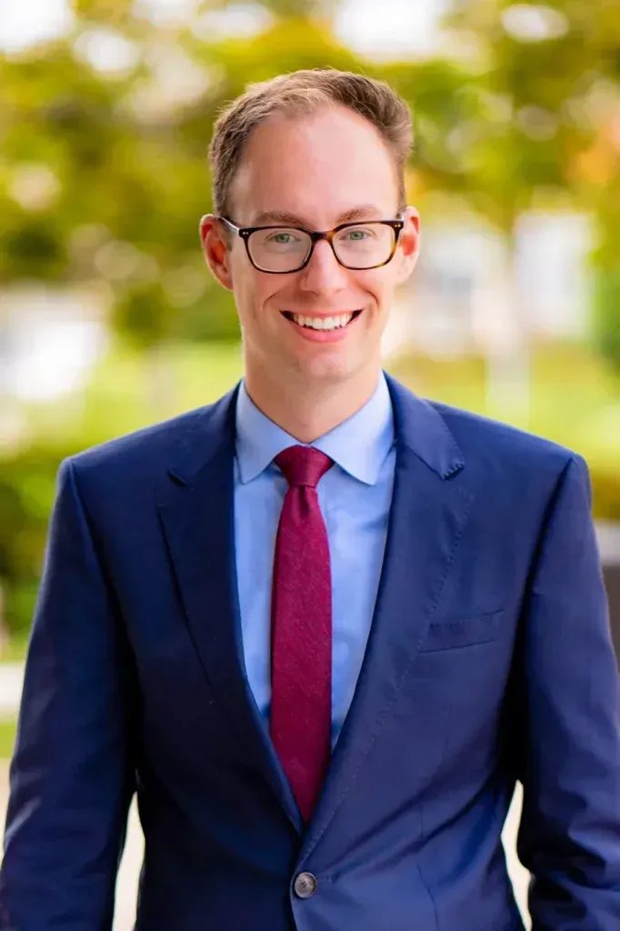 A man with a high hairline in a suit and tie is smiling for the camera.