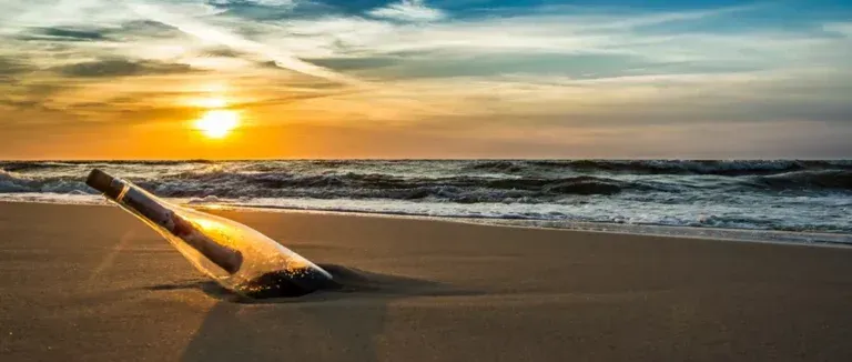 A message in a bottle is laying on the beach at sunset.