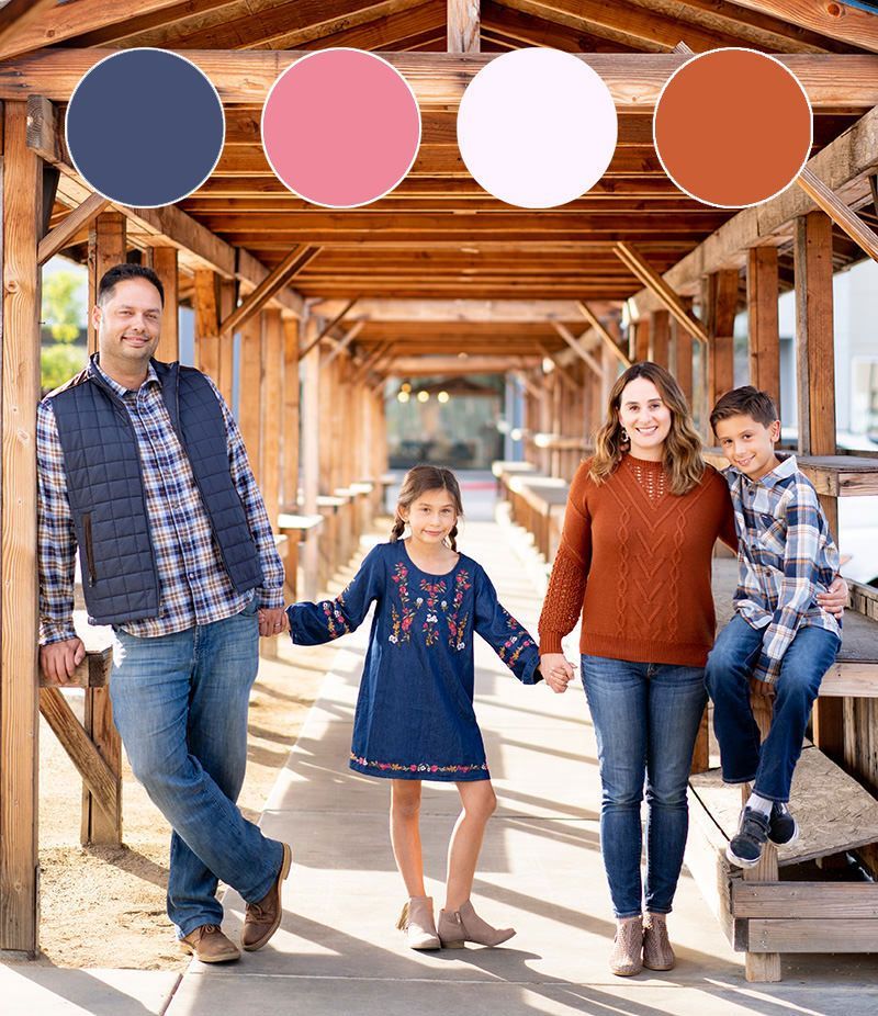 A family is standing under a wooden structure holding hands.