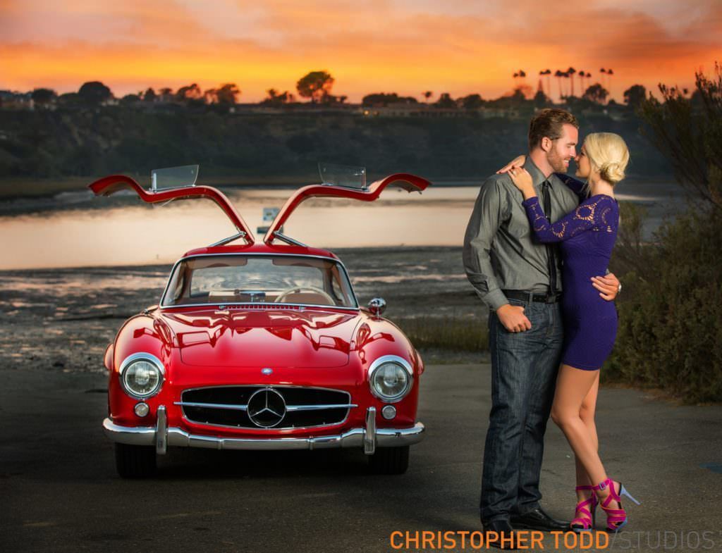 A man and woman are kissing in front of a red mercedes in Newport Beach