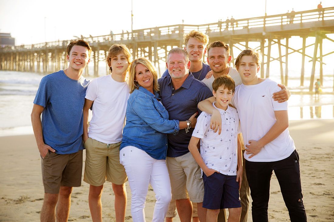 A large family is posing for a picture on the beach in front of the Newport Beach Pier. 