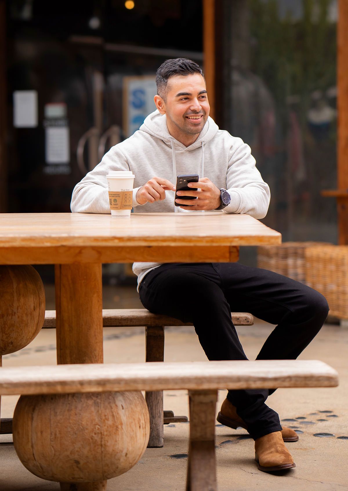 A man is sitting at a table with a cup of coffee and a cell phone for a professional dating photo.