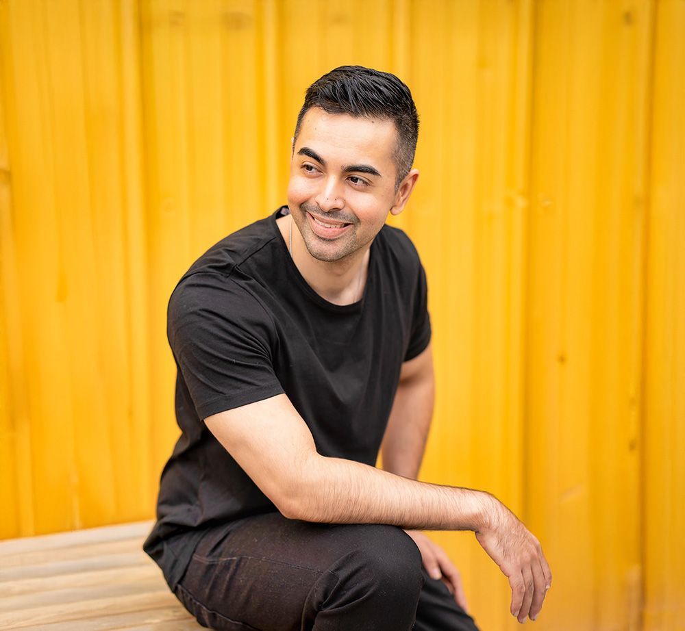 A man in a black shirt is sitting on a bench in front of a yellow wall.