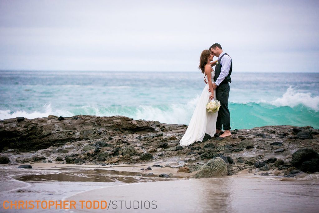 A bride and groom kissing on a rocky beach at Shaws Cove In Laguna Beach