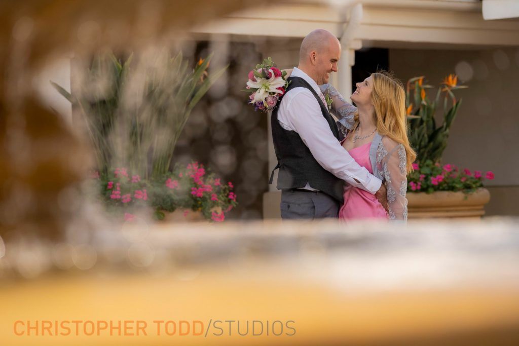 A bride and groom are posing for a picture in front of a fountain.