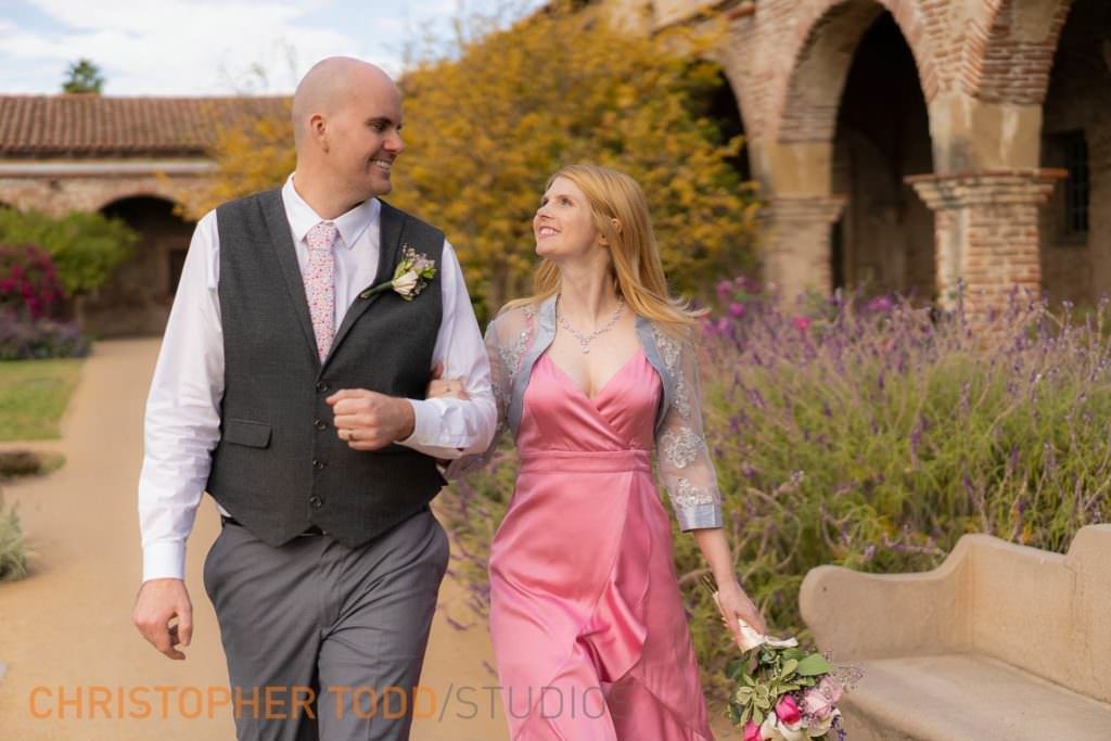 A Bride and Groom are walking down a path at the MIssion San Juan Capistrano
