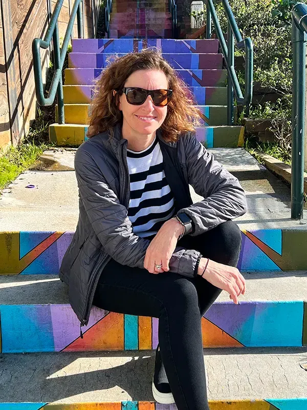A woman wearing sunglasses is sitting on a set of colorful stairs.