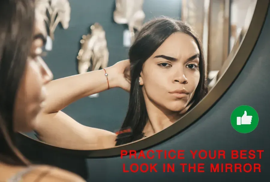 A woman is looking at her reflection in a mirror to practice facial expressions for a headshot