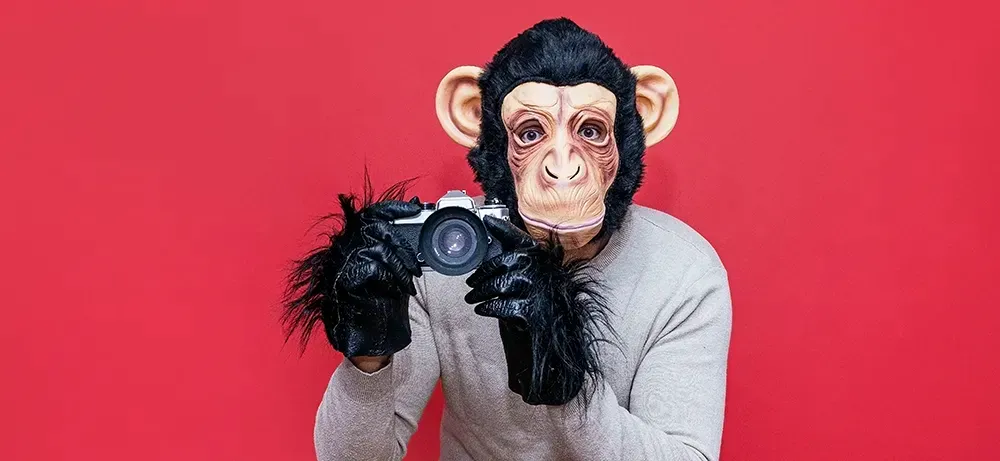 A man wearing a monkey mask is taking a picture with a camera.