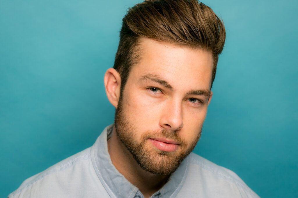 A male model with a beard is wearing a blue shirt and looking at the camera.