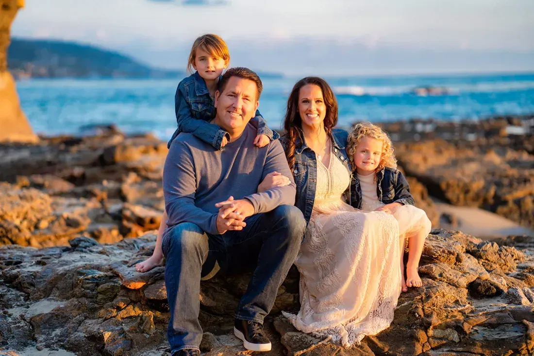 A family is posing for a picture on a rocky beach.