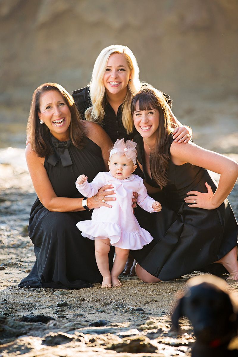 Three women and a baby are posing for a picture on the beach.