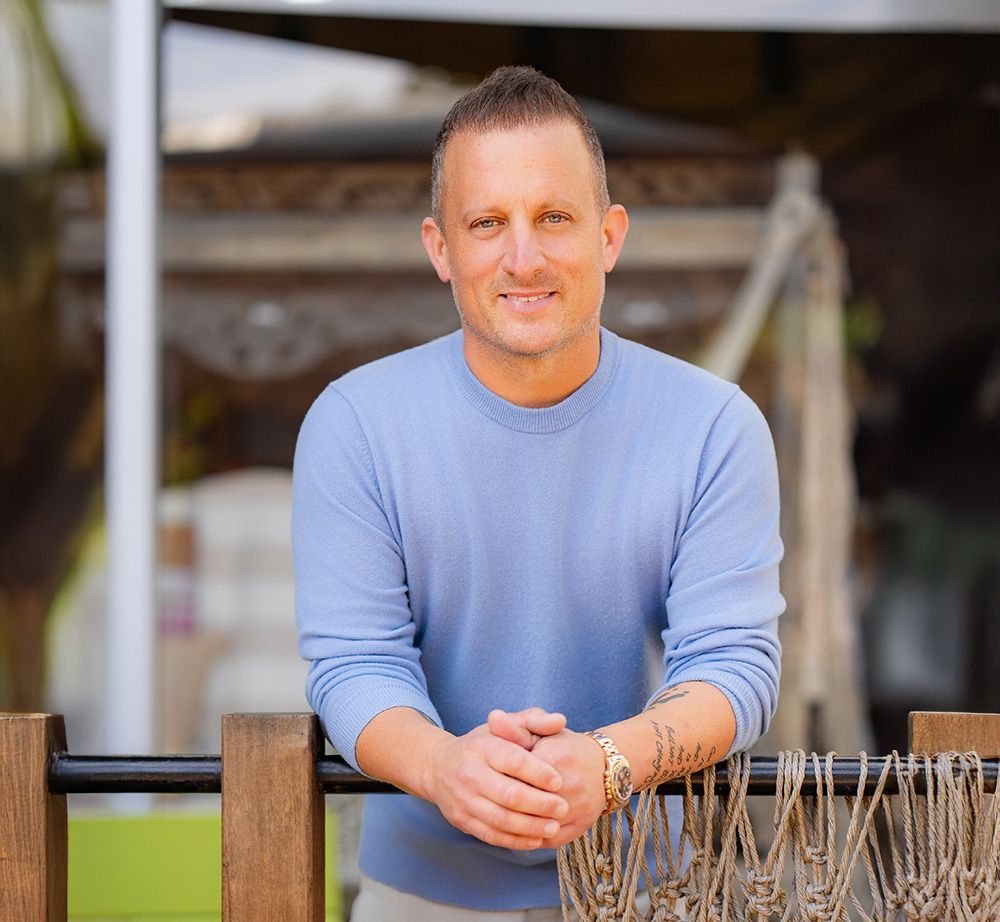 A man in a blue sweater is leaning against a wooden fence.