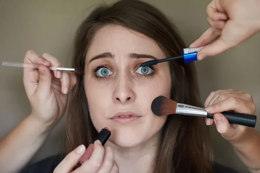 A stressed woman is getting her makeup done by a group of people.