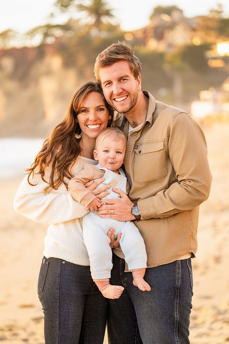 A man and woman are holding a baby on the beach.