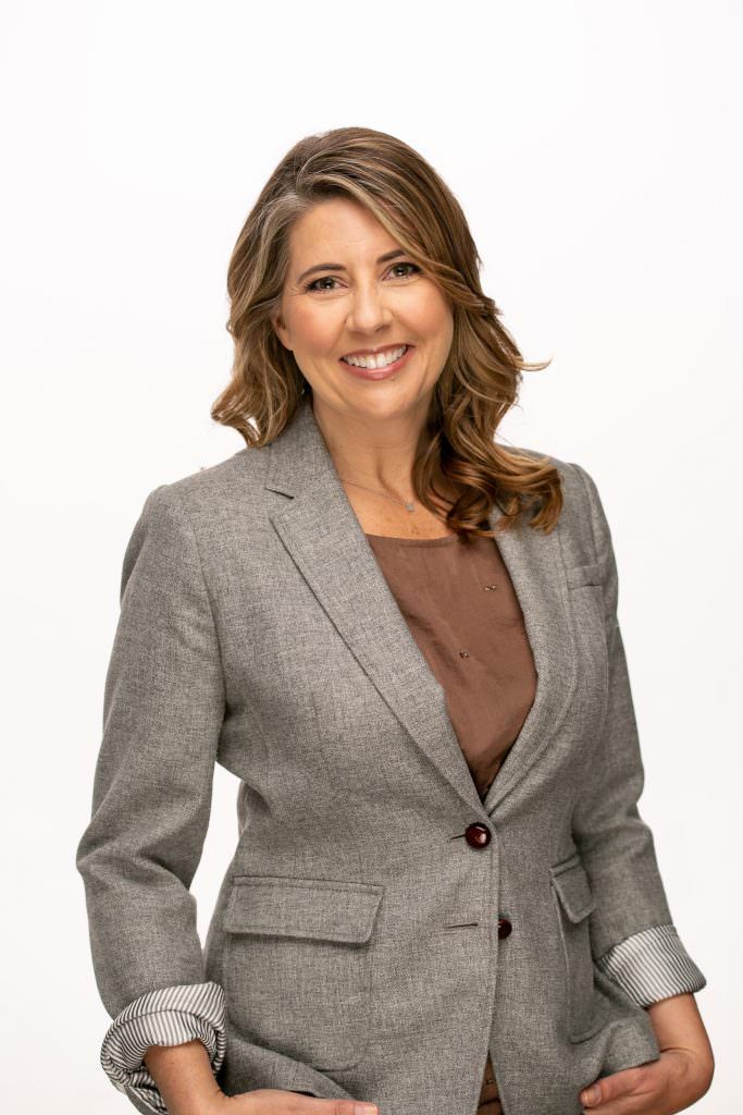 A woman in a grey jacket and brown shirt is smiling for the camera.