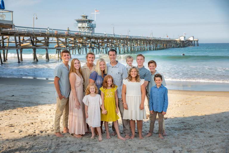 A large family is posing for a picture on the beach in front of San Clemente pier.